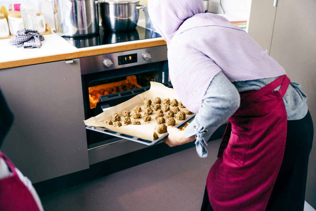 A member of Healthy Living Platform putting homemade falafels into an oven,